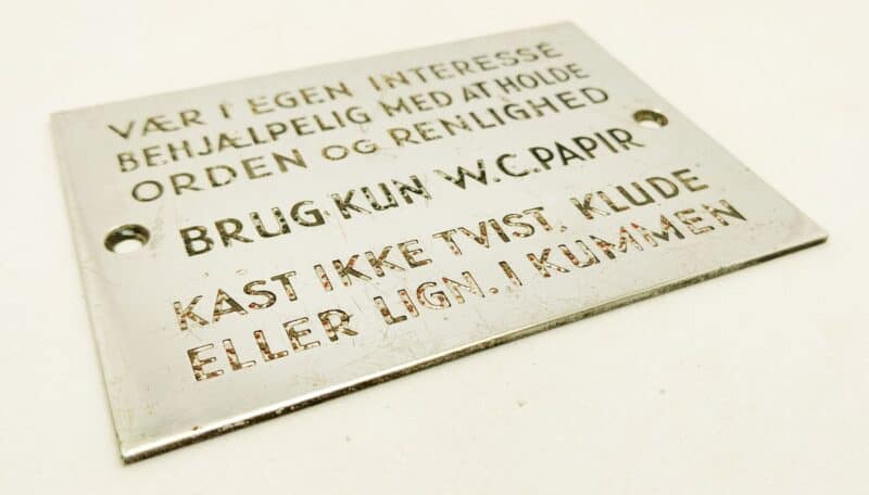 Metalskilt. Vær i egen interesse behjælpelig med at holde orden og renlighed. BRUG KUN W. C. PAPIR. Kast ikke tvist, klude eller lign. i kummen