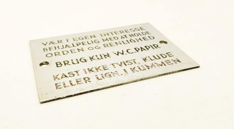 Metalskilt. Vær i egen interesse behjælpelig med at holde orden og renlighed. BRUG KUN W. C. PAPIR. Kast ikke tvist, klude eller lign. i kummen