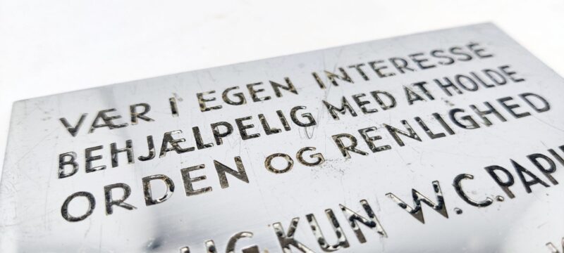 Metalskilt. Vær i egen interesse behjælpelig med at holde orden og renlighed. BRUG KUN W. C. PAPIR. Kast ikke tvist, klude eller lign. i kummen