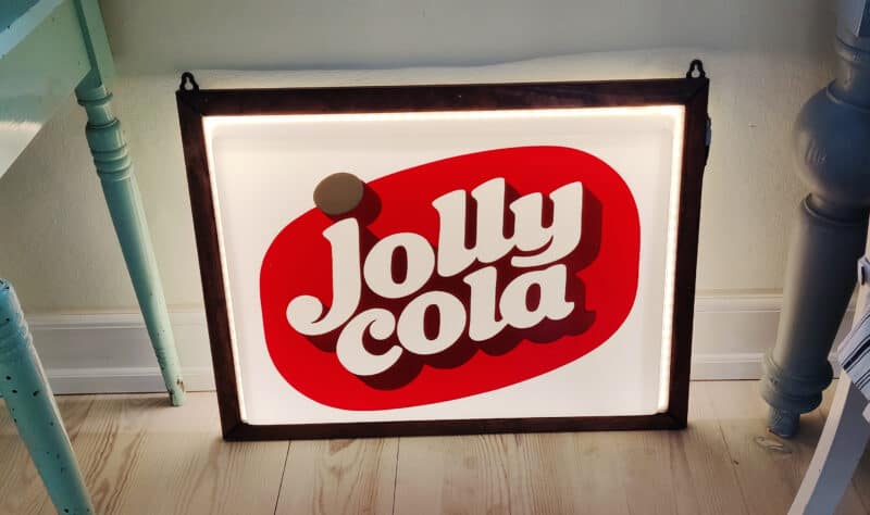 Jolly Cola lysskilt i plast. I træramme