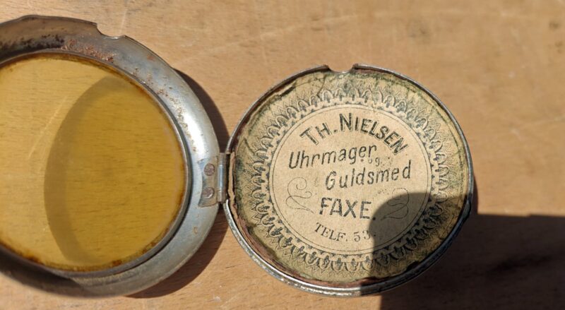 Th. Nielsen. Uhrmager og guldsmed Faxe.  Telf. 53. Blikdåse itui til lommeur med reklame